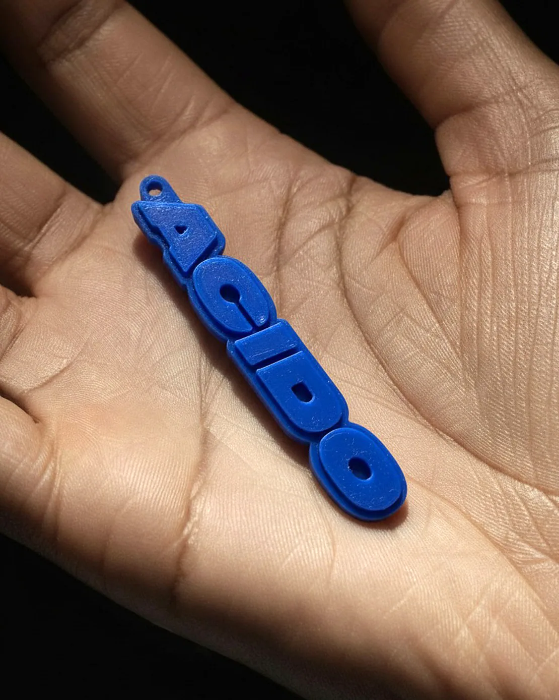 Portachiavi blu con scritta ACIDO posizionato su palmo di una mano aperta