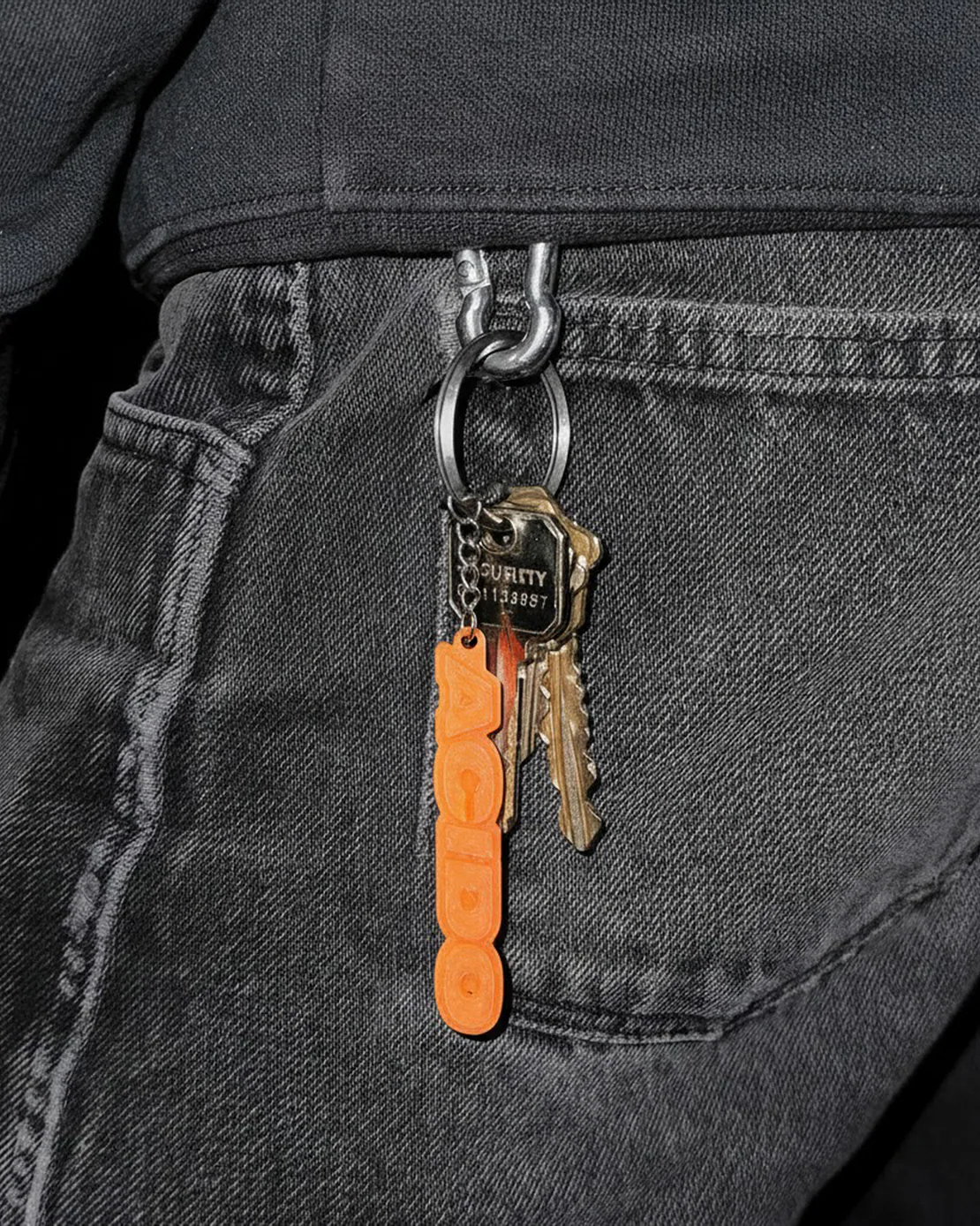 Portachiavi traslucido arancione con scritta ACIDO con mazzo di chiavi agganciato a jeans neri
