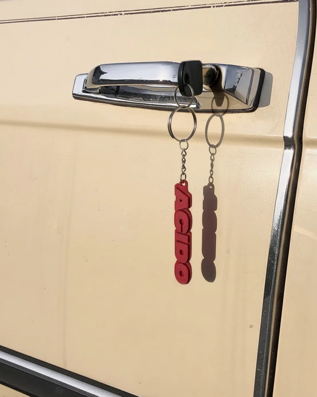 Portachiavi rosso con scritta ACIDO agganciato a chiave inserita su portiera di una macchina