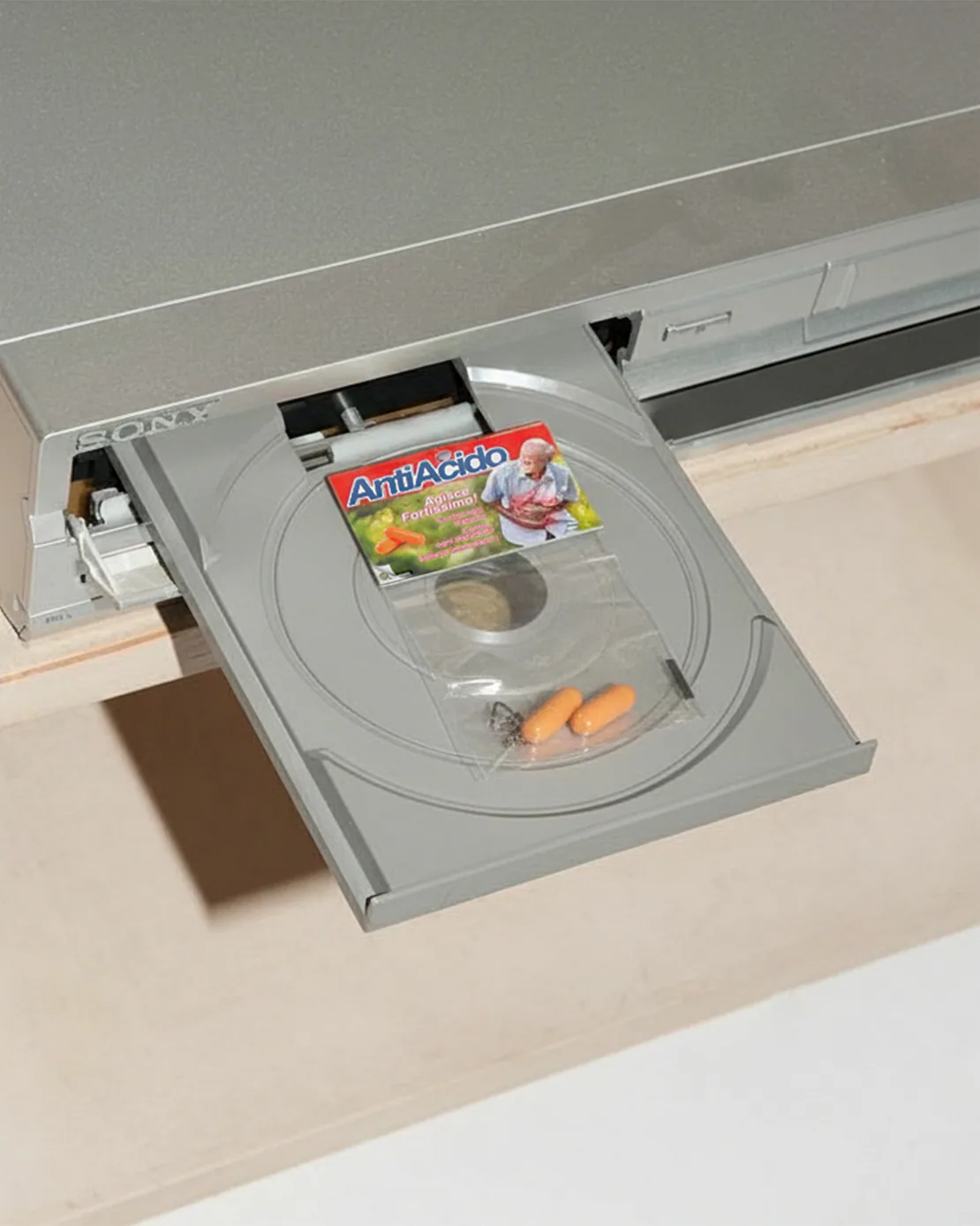 Confezione di Antiacido Pills inserita nel vassoio aperto di un lettore CD/DVD grigio Sony.