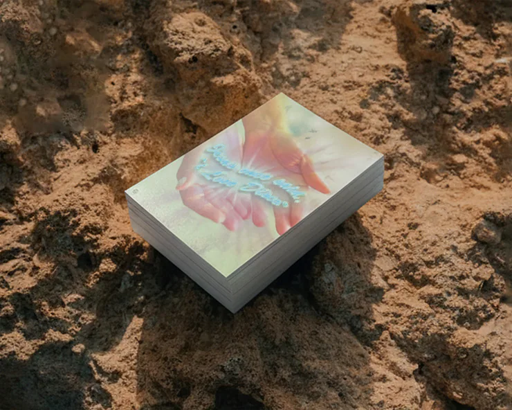 Mazzo di cartoline poggiato su una roccia, con immagine di mani giunte che emanano luce e testo decorativo Jesus still loves Disco.