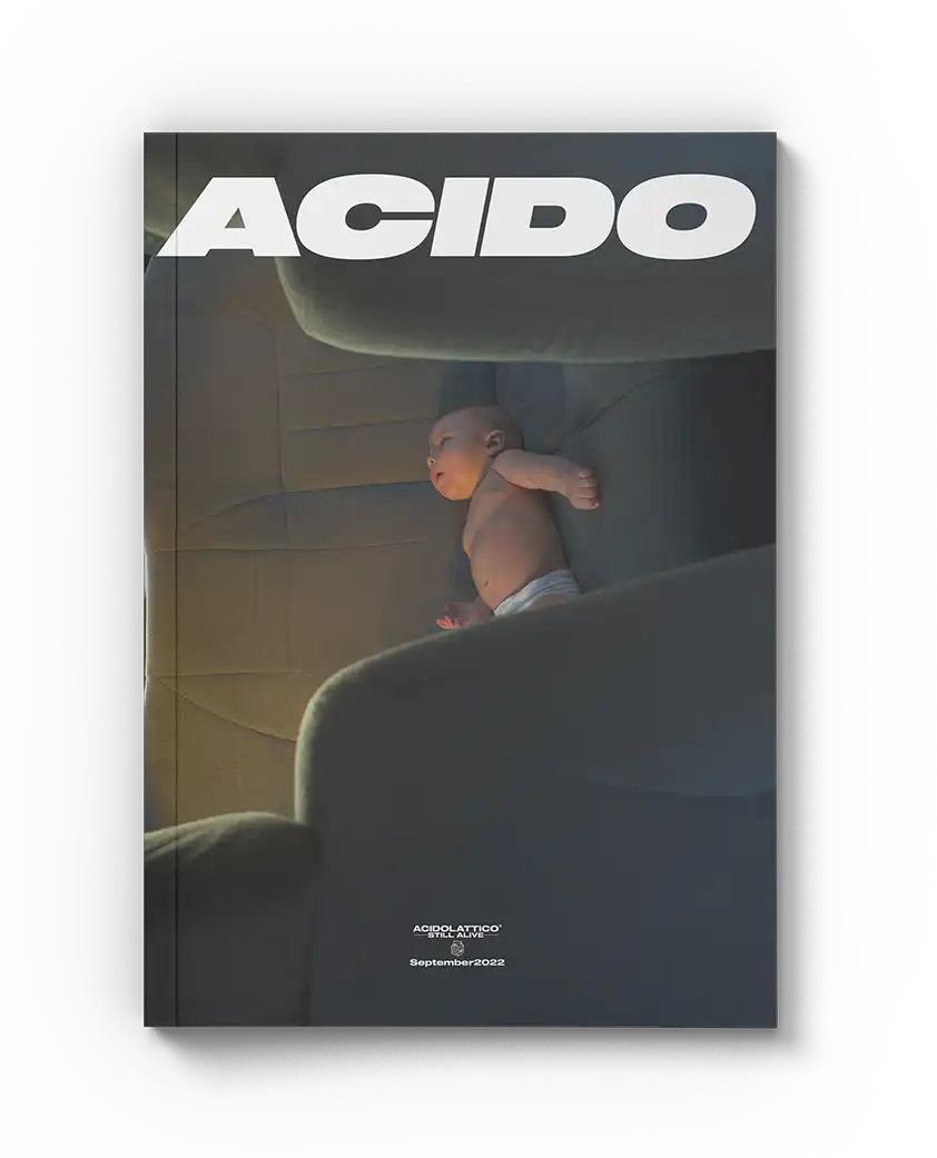 Copertina della rivista con il titolo 'ACIDO' in bianco, un neonato sdraiato su una poltrona scura, e la scritta 'Still Alive - September 2022' in basso.