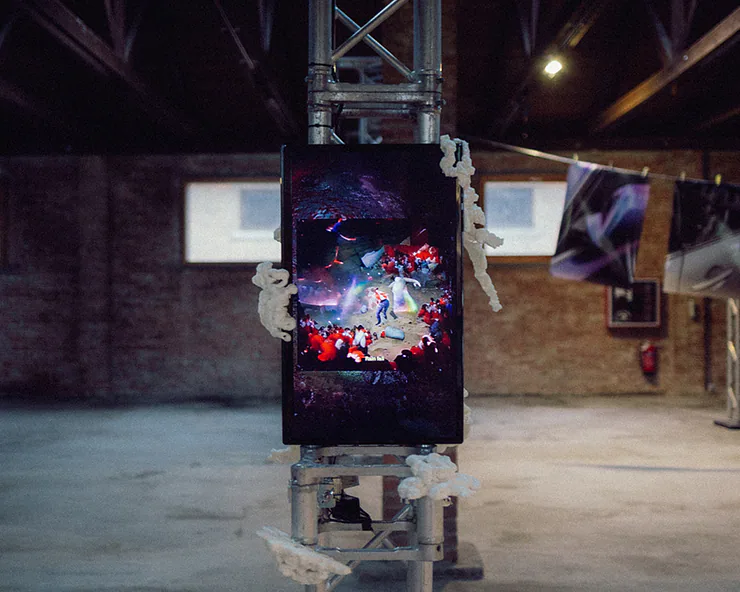 Installazione di video arte con uno schermo verticale montato su una struttura metallica ed elementi scultorei.