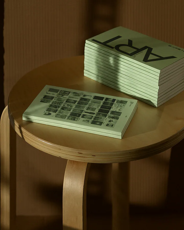 Pile del catalogo di arte Artefici esposte su uno sgabello di legno, illuminate dalla luce del sole.