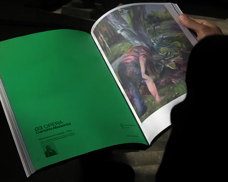 Una persona vista di schiena mentre sfoglia il catalogo Artefici, mostrando la pagina dedicata all'artista Carlotta Mazzariol.