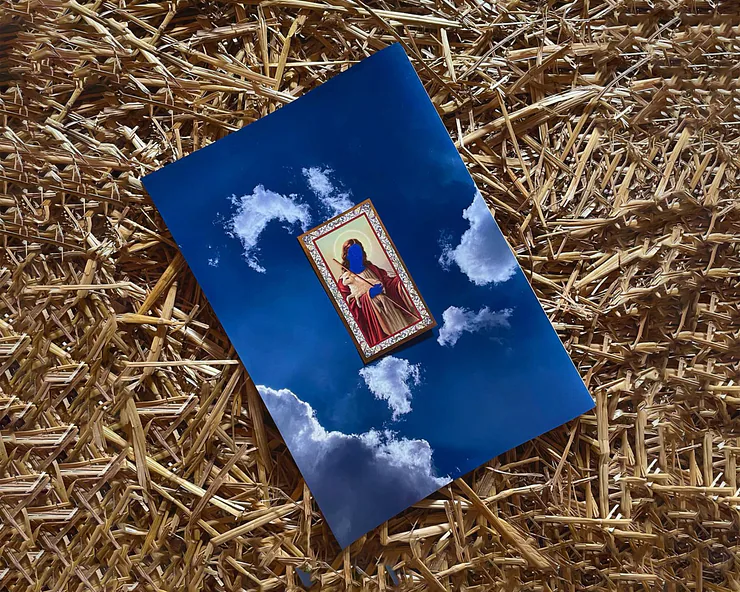 Una stampa di arte appoggiata sulla paglia, raffigurante una icona sacra con il volto coperto di blu su uno sfondo di cielo.