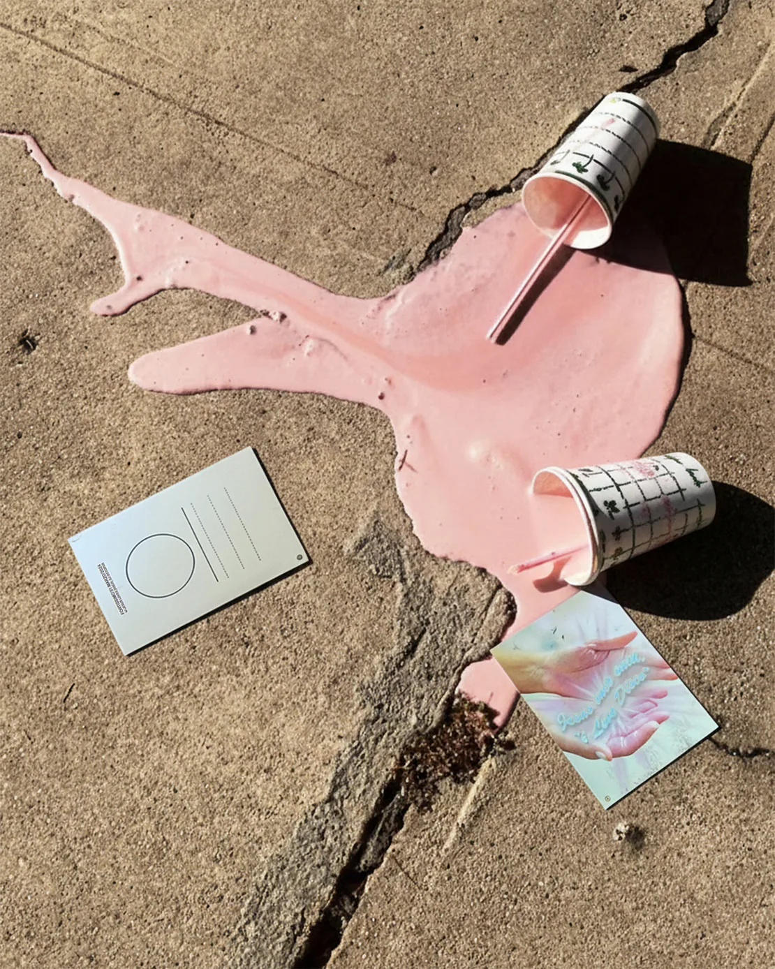Cartolina “Jesus Loves Disco” accanto a due milkshake rovesciati sul marciapiede.
