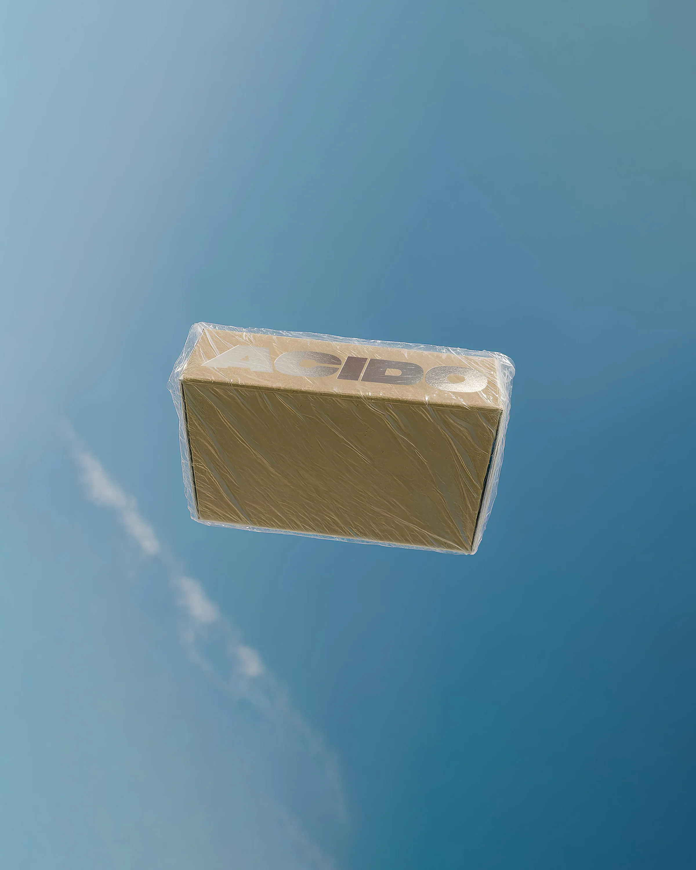 Cofanetto rettangolare avvolto in plastica trasparente con la scritta ACIDO sul lato superiore, fotografata contro un cielo azzurro limpido