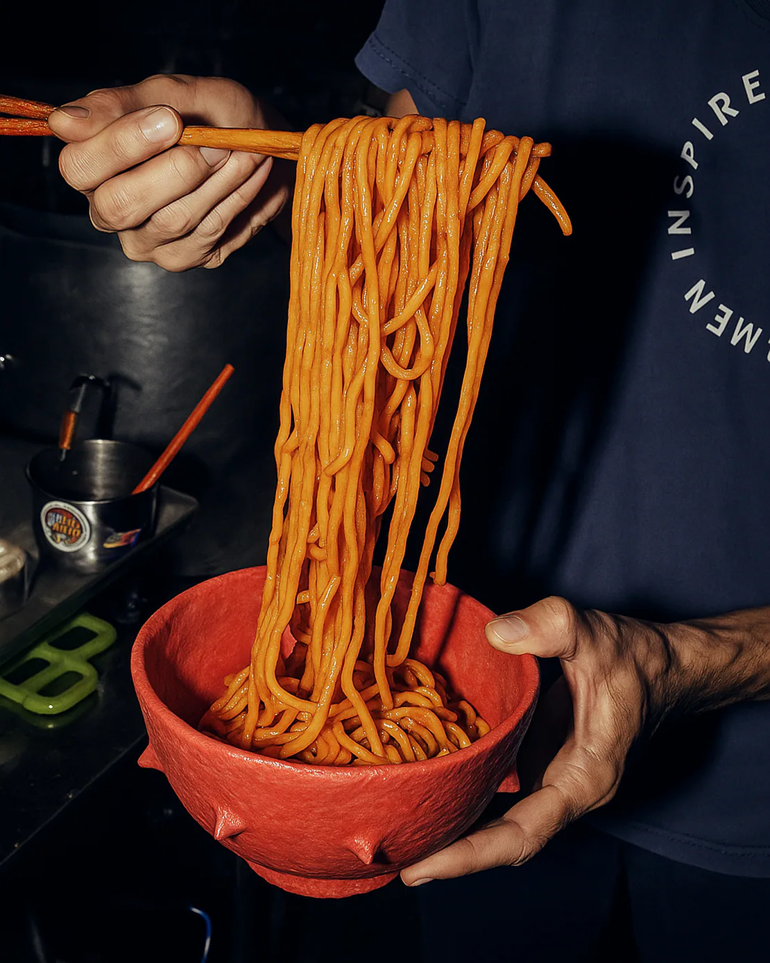 Persona che solleva spaghetti con bacchette sopra una ciotola rossa per ramen in ceramica.