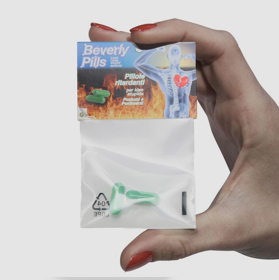 Confezione di Beverly Pills tenuta in mano con smalto rosso, evidenziando il design ironico e i dettagli grafici del prodotto.
