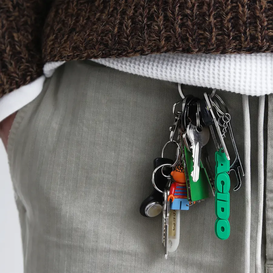 Portachiavi verde 'ACIDO' appeso a un mazzo di chiavi e fissato a un paio di pantaloni in jeans.