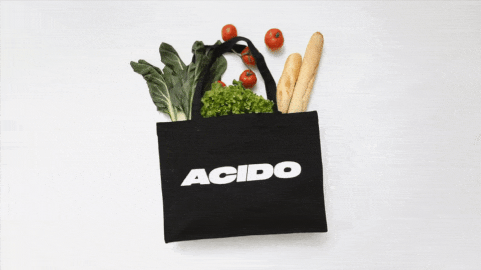 GIF che mostra la totebag nera 'ACIDO' riempita con verdure fresche, pomodori e baguette che esplode.