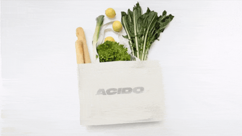 GIF animata della Totebag bianca 'ACIDO' con brillantini, riempita con verdure fresche e pane.
