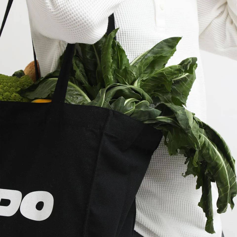 Dettaglio della totebag nera che mostra una cucitura ben rifinita, il tessuto resistente e della verdura che fuoriesce.
