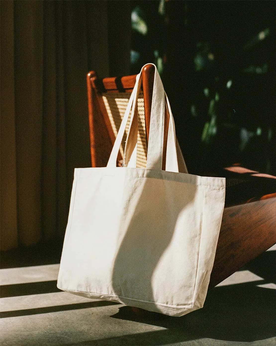 Retro totebag bianca appoggiata su una sedia in legno illuminata dalla luce naturale.