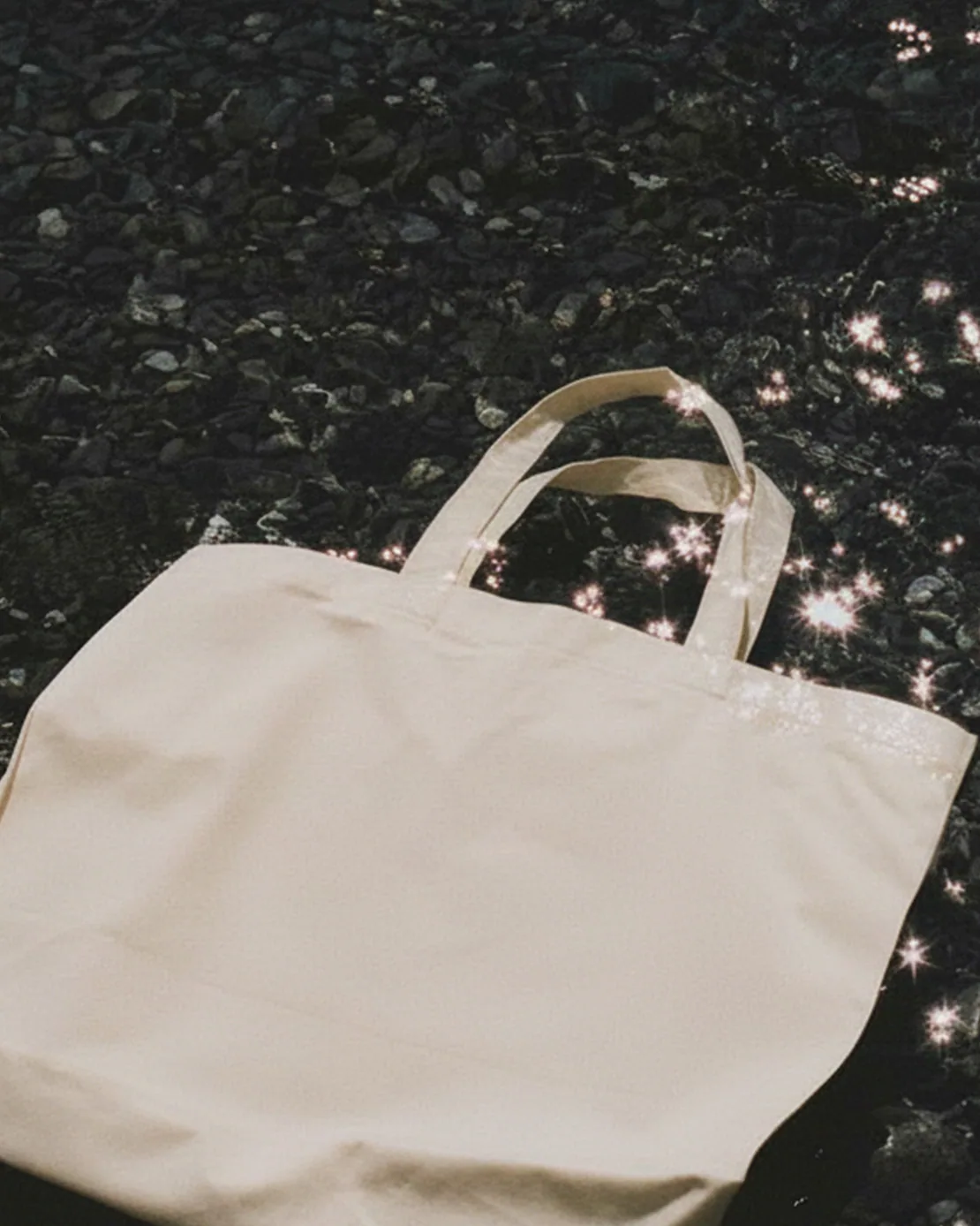 Totebag bianca ACIDO distesa a terra accanto a una rivista con copertina blu.